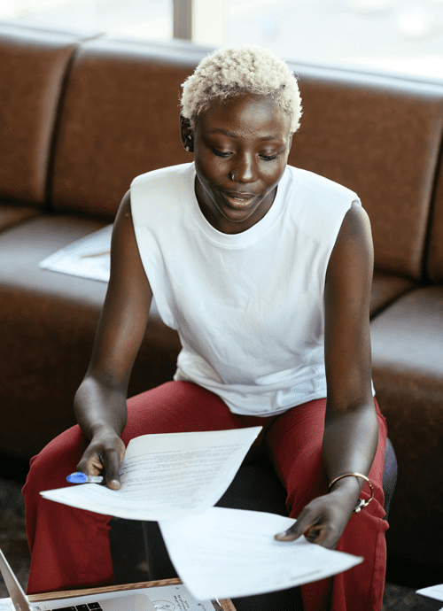 Woman sits on an ottoman in front of a leather couch and holds documents